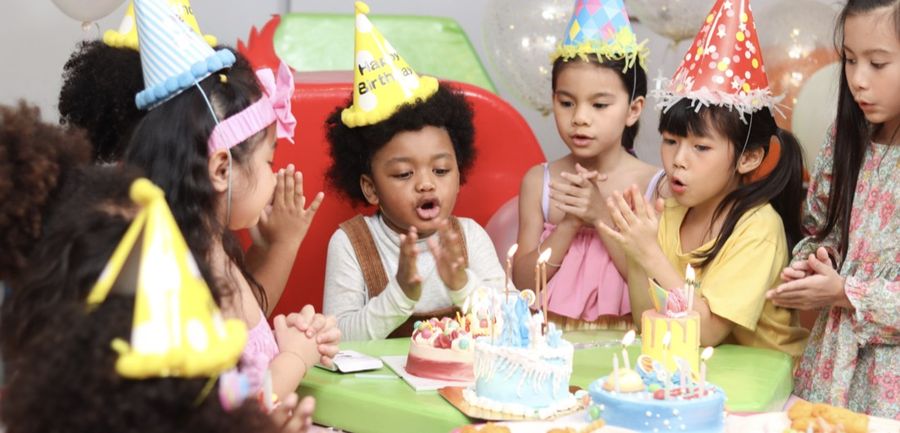 Enfants avec chapeaux de fête soufflant les bougies autour de gâteaux